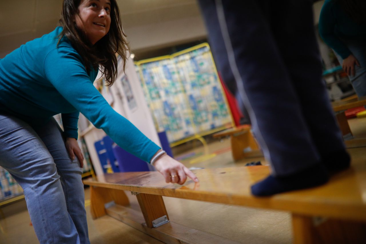 Una fisioterapeuta ayuda a uno de sus alumnos a mantener el equilibrio sobre un banco.