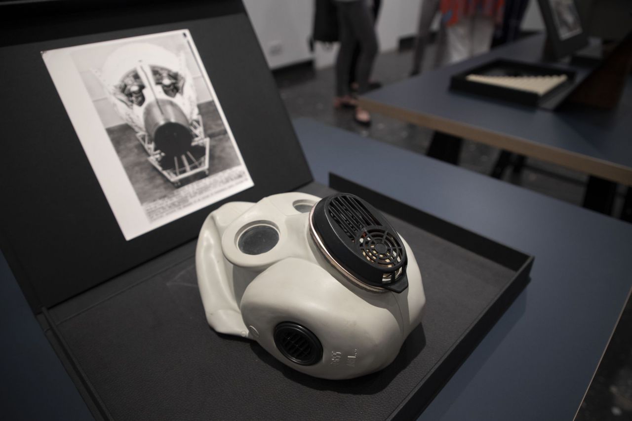 Una máscara entre los objetos expuestos y fotografiados en la exposición.
