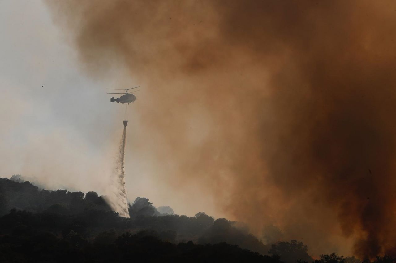Un helicóptero trata de apagar el incendio entre grandes nubes de humo.