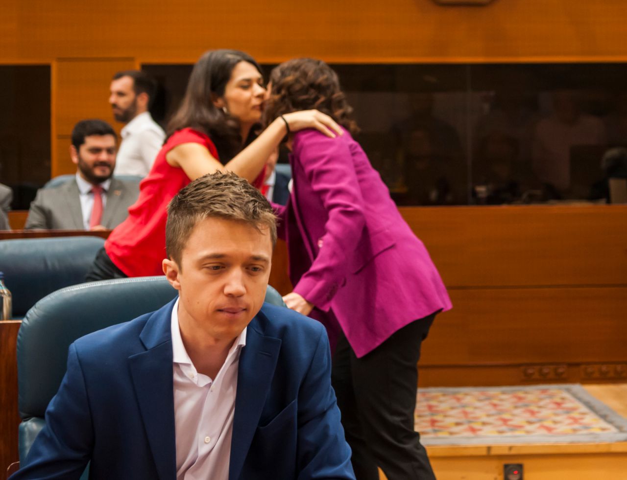 Saludo entre Isa Serra (Podemos) e Isabel Díaz Ayuso (PP). En primer plano, un concentrado Íñigo Errejón (Más Madrid)