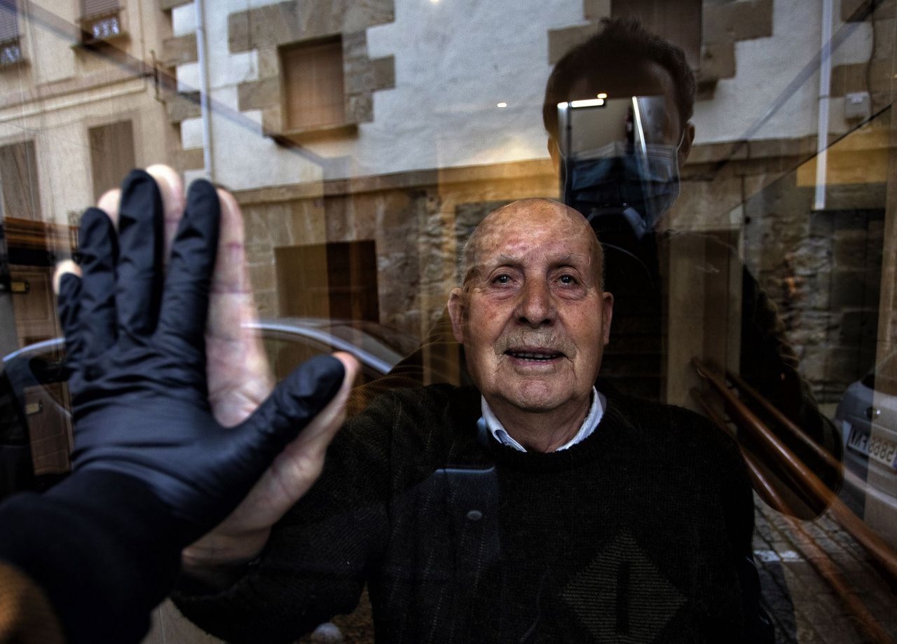 Visita a mi abuelo Miguel, de 90 años, durante el confinamiento que saluda a través del cristal del portal. El alto índice de personas mayores afectadas por la Covid-19 les obligó a un estricto aislamiento con la esperanza de evitar el contagio. Huarte, Navarra, 1 de abril, 2020