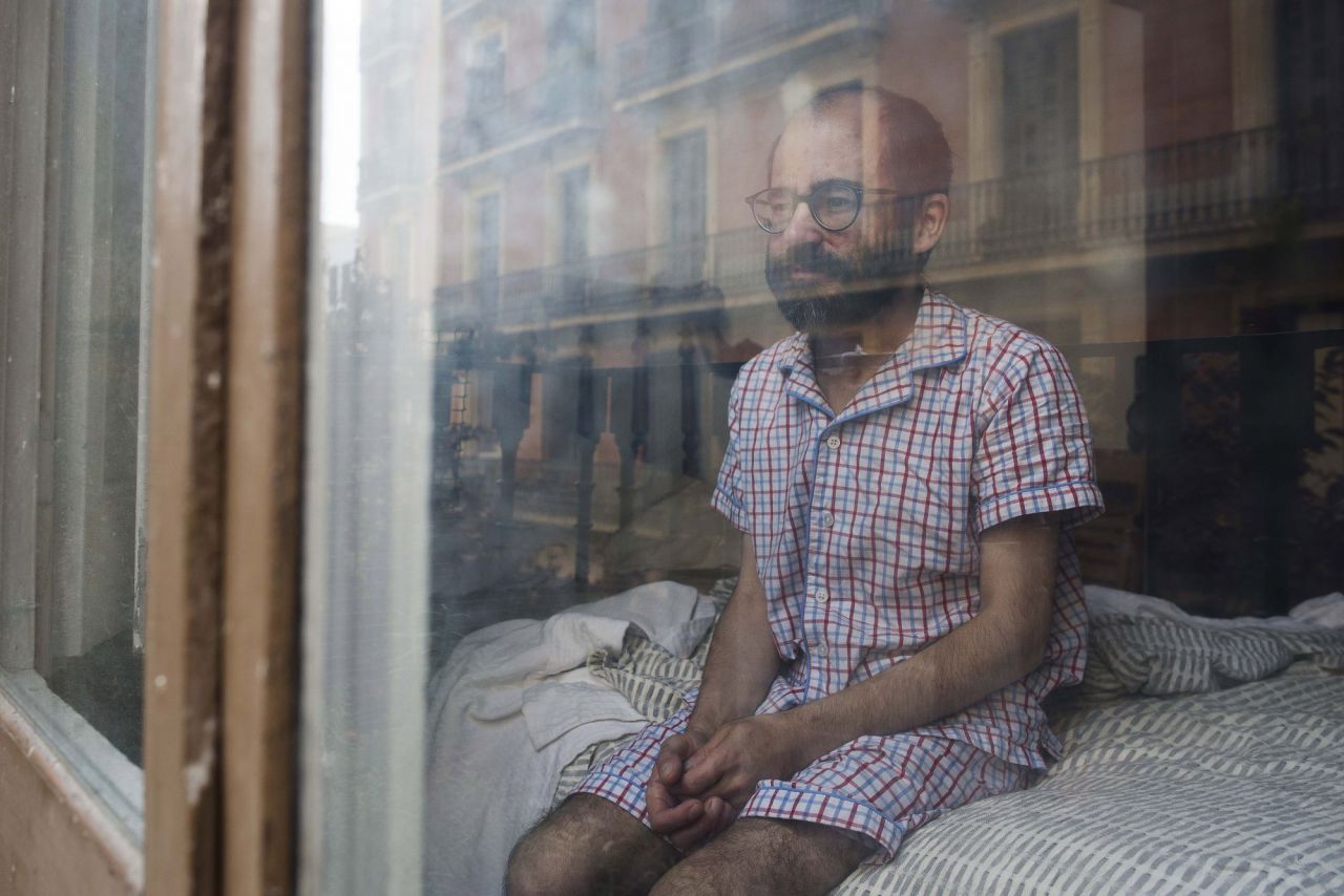 Joan sentado en la cama tras despertarse en Barcelona. Son meses en los que pensamos mucho sobre lo que estamos viviendo. De hecho, los dos hemos cogido la costumbre de trasladar lo que vivimos en nuestros diarios personales. Por ejemplo, Joan, escribe el 23 de marzo: “Comienza una nueva semana de confinamiento que cada vez se hace más complicado. Wayra ha salido a la calle a comprar y, como cada vez, vuelve preocupada por la posibilidad de haber traído el maldito virus a casa. Mantener la calma en un momento sin certidumbres ni seguridades es muy complicado, y nos puede llevar a caer en la tentación de la preocupación excesiva.” Barcelona, 30 de mayo, 2020. 