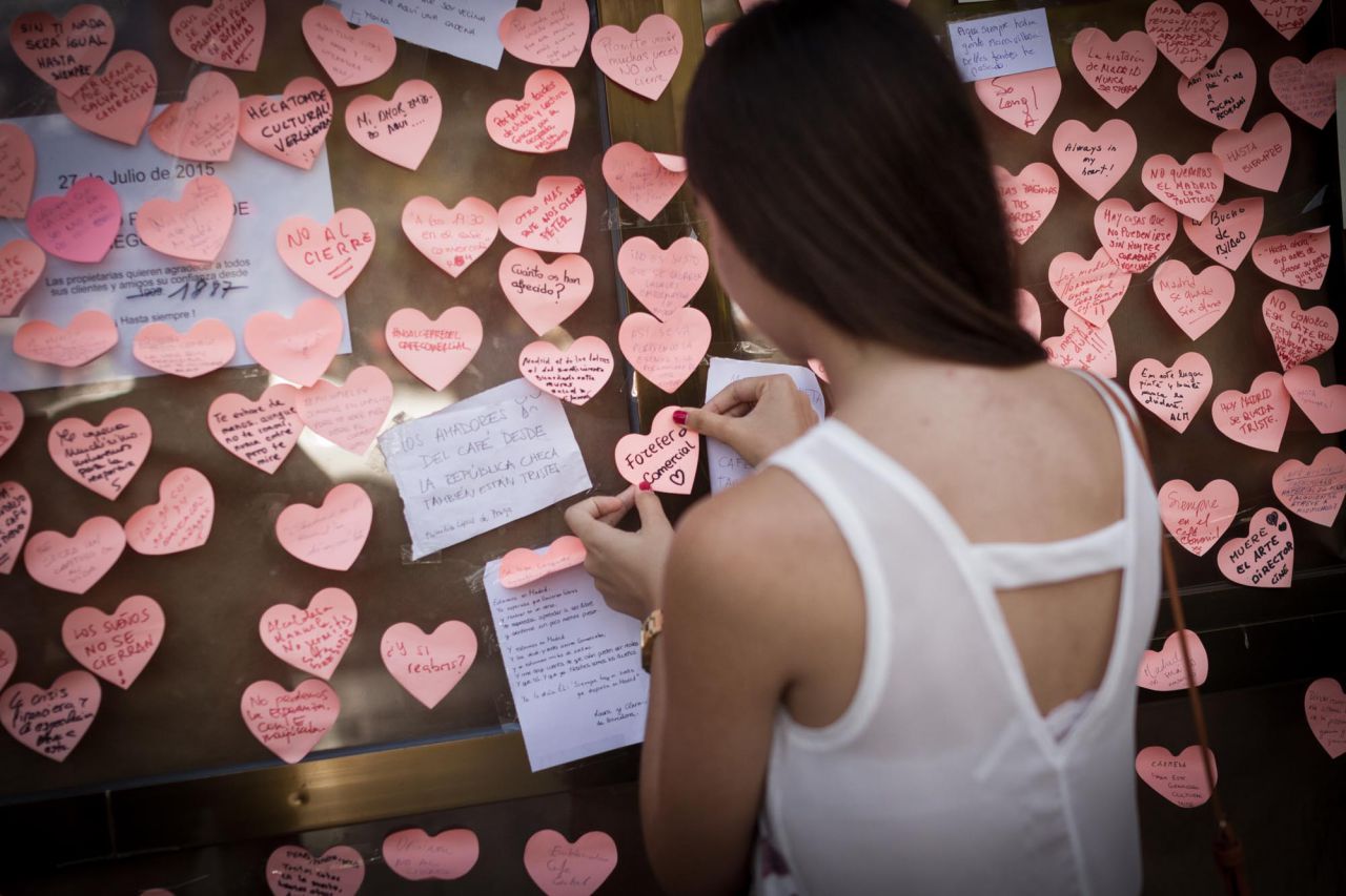 Una mujer pega un corazón de papel en uno de los escaparates del Café Comercial con el lema 