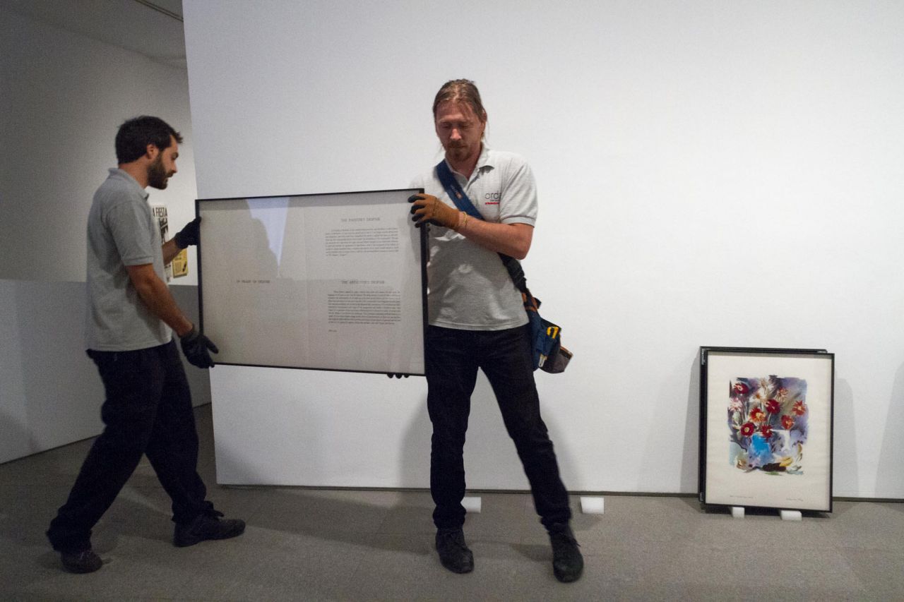 Dos operarios trasladan una obra para ubicarlas en una nueva exposición.