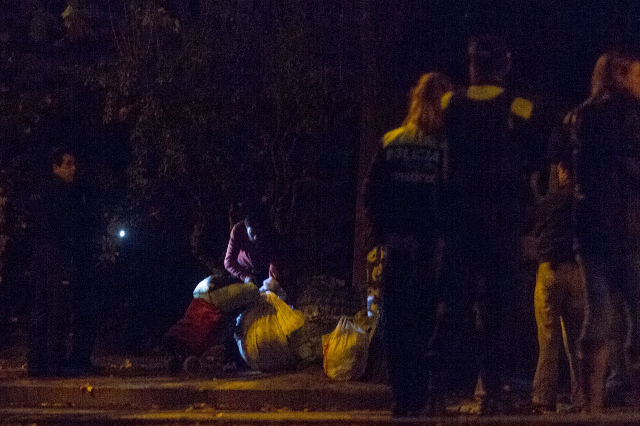 Un policía municipal alumbra a uno de los ocupantes para que pueda ver sus pertenencias.