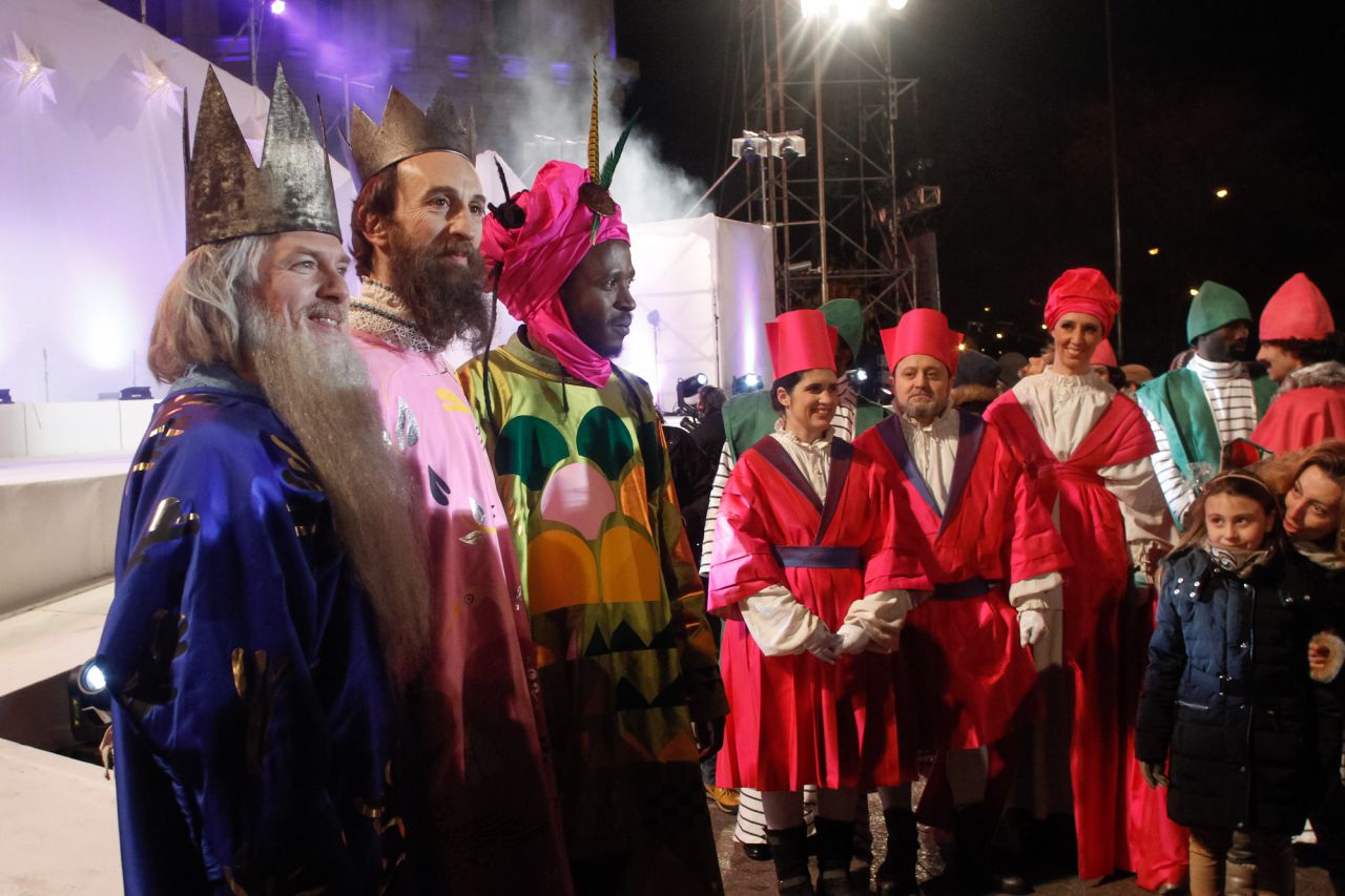 Los tres Reyes Magos posan ante los medios observados bajo la atenta mirada de una niña y su madre.