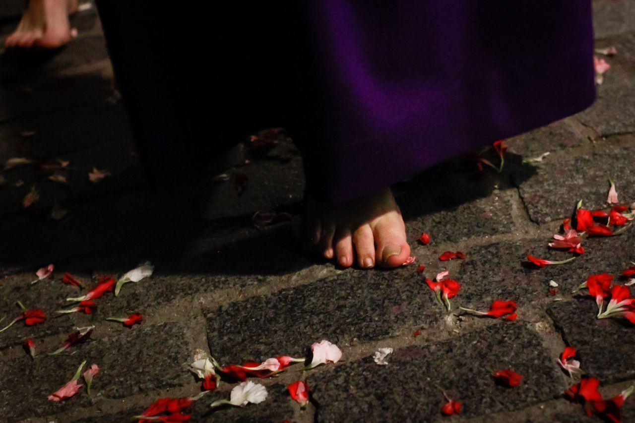 Un penitente descalzo avanza pisando los pétalos de flores.