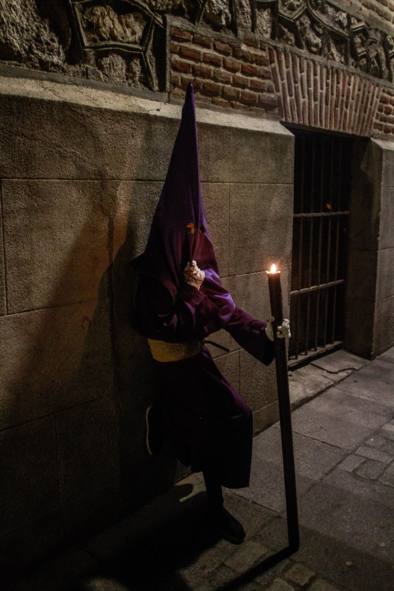Un penitente que porta un cirio descansa apoyado en la pared de la calle del Cordón.