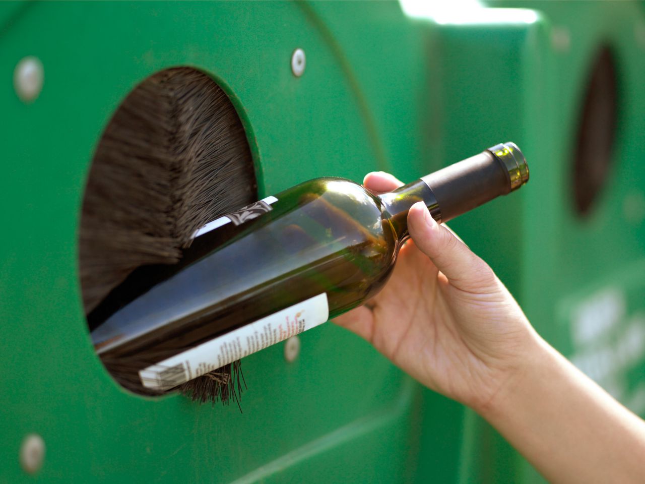 Una persona deposita una botella de vidrio en el contenedor verde