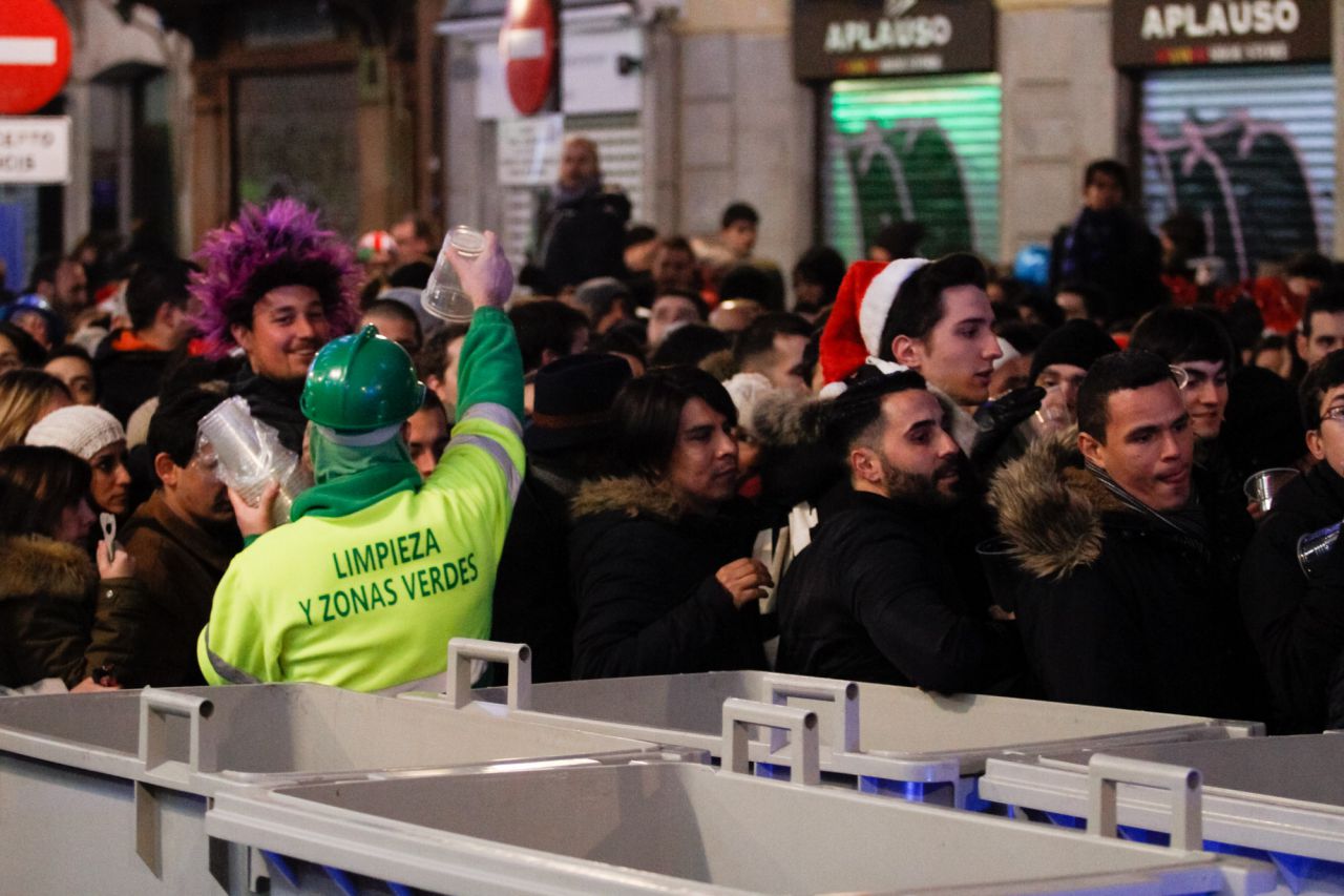 Un operario de la limpieza de Madrid da vasos de plástico a las personas que quieren acceder a la Puerta del Sol para celebrar la Nochevieja 2017.