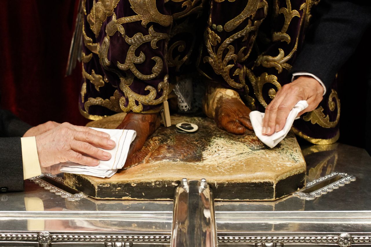 Dos hermanos de la cofradía limpian los pies de la imagen de Jesús tras ser besada por los feligreses.