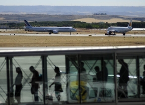 Una fila de viajeros en un finger a la espera de abordar su avión en el aeropuerto de Madrid-Barajas, al fondo aviones en la pista.