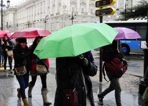 un grupo de jovenes turistas con paraguas por la fina lluvia en Madrid