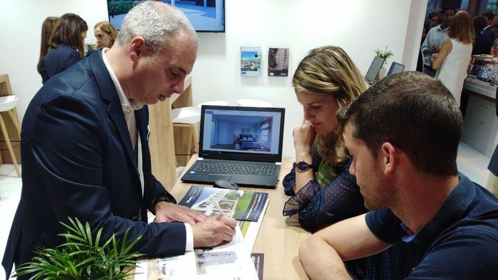 Un comercial de AEDAS Homes atiende a dos visitantes en el SIMA 2019.