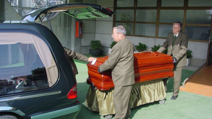 Trabajadores de la empresa mixta de servicios funerarios metiendo un féretro en un coche fúnebre.