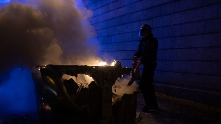 Un agente trata de apagar un contenedor incendiado en las protestas de Ferraz