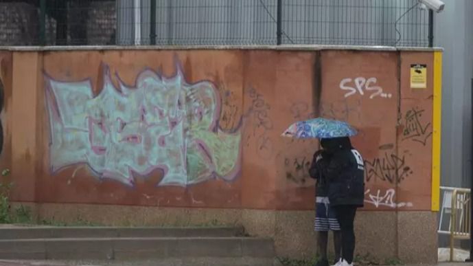 Dos migrantes se protegen de la lluvia con un paraguas en las inmediaciones del centro de Emergencia Acogida y Derivación en el Acuartelamiento 'Primo de Rivera', donde se alojan migrantes procedentes de Canarias, a 19 de enero de 2024, en Alcalá de Henares