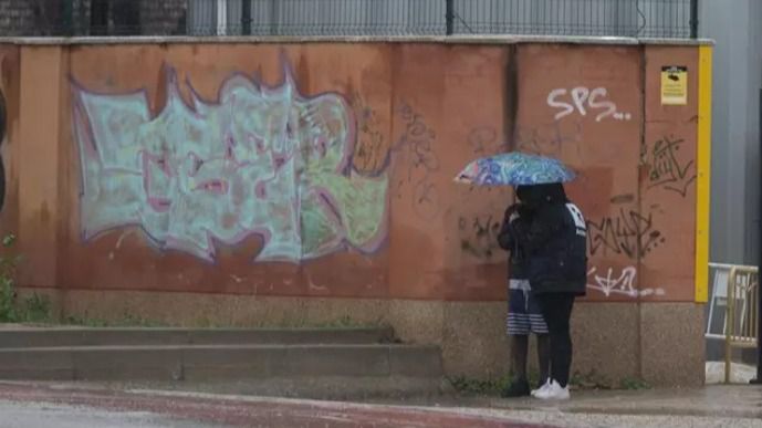 Dos migrantes se protegen de la lluvia con un paraguas en las inmediaciones del centro de Emergencia Acogida y Derivación en el Acuartelamiento 'Primo de Rivera', donde se alojan migrantes procedentes de Canarias, a 19 de enero de 2024, en Alcalá de Henares