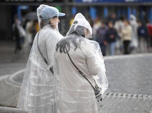 Dos viandantes con chubasquero se resguardan de la lluvia en Madrid