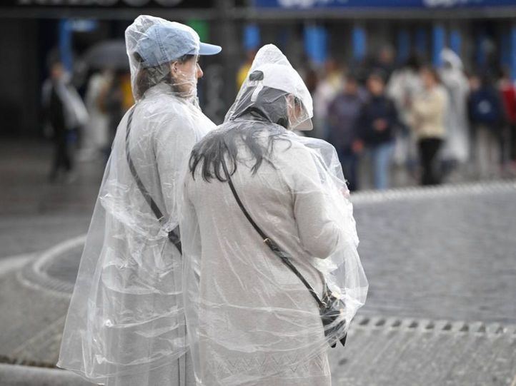Dos viandantes con chubasquero se resguardan de la lluvia en Madrid