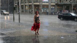 Una mujer con el vestido recogido camina bajo la lluvia en una tormenta veraniega por Gran Vía.
