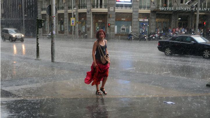 Una mujer con el vestido recogido camina bajo la lluvia en una tormenta veraniega por Gran Vía.