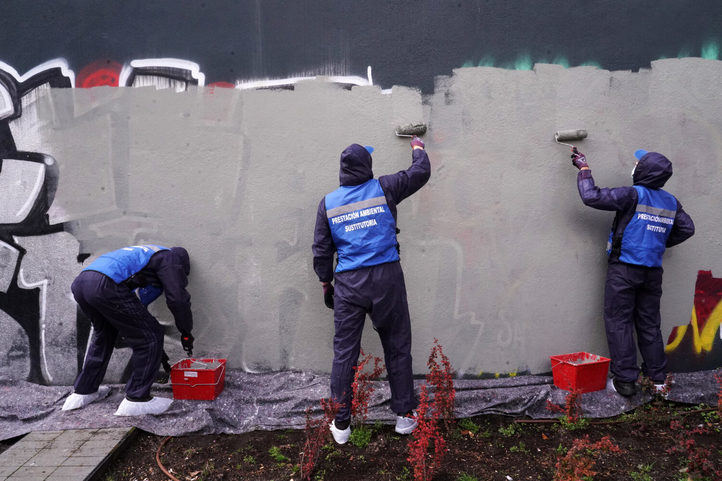 Tres de los grafiteros que conmutan su multa cubriendo las pintadas de un muro en la plaza de Juan Muñoz